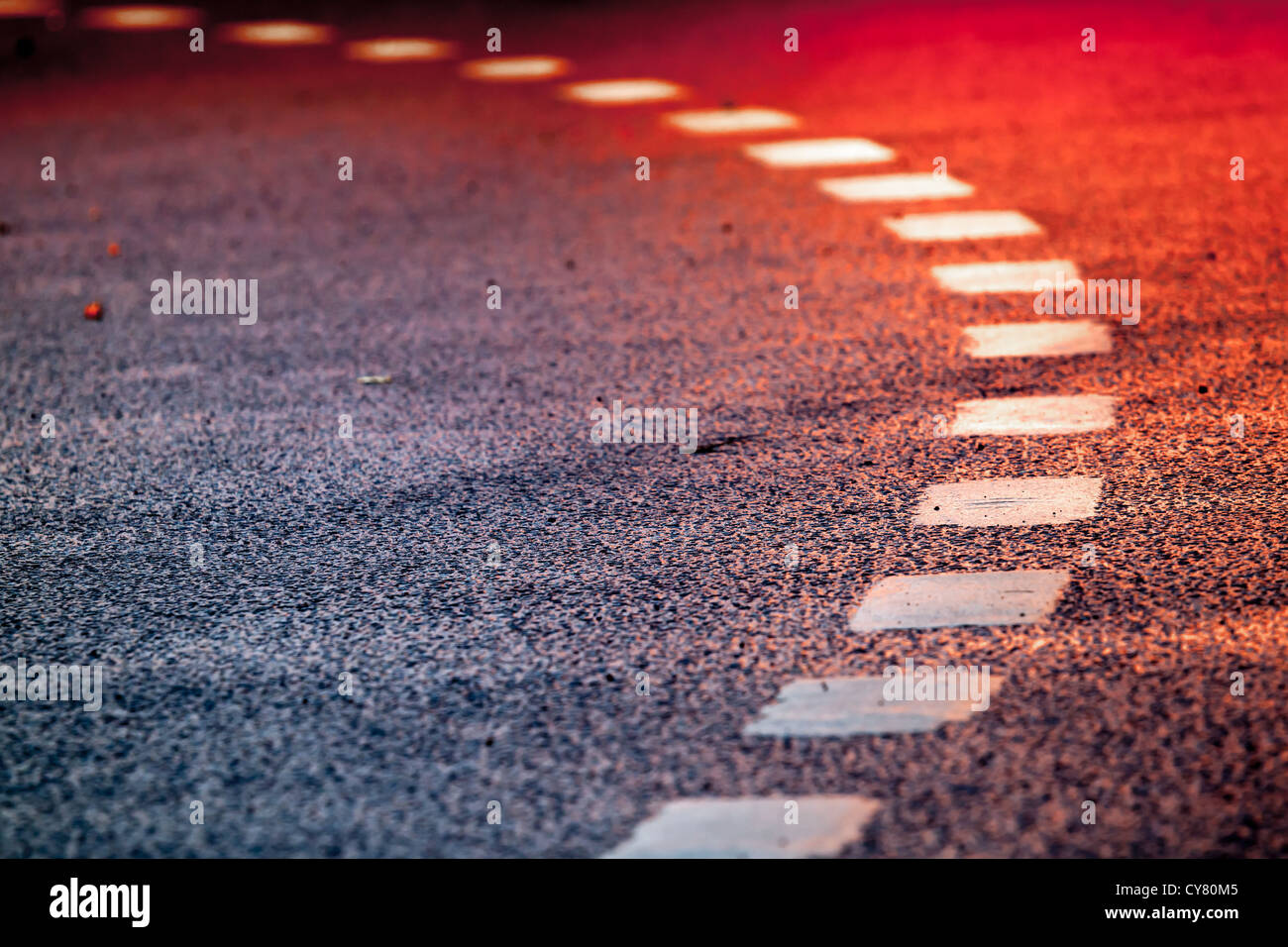 Asphaltstraße mit Kennzeichnung von Linien und helle rote Reflexionen drehen Stockfoto