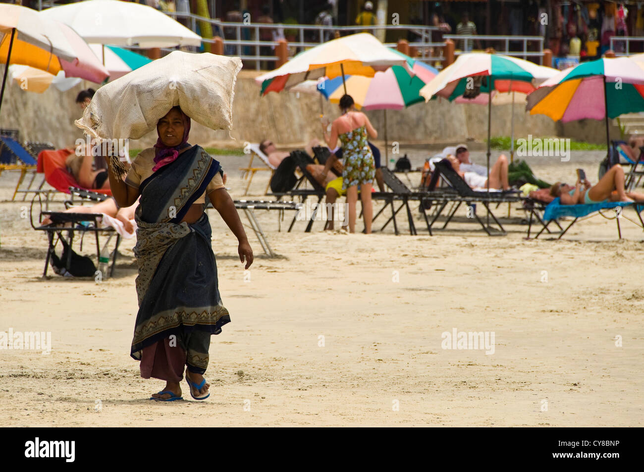 Horizontale Ansicht einer indischen Frau, die mit einer Tasche von Müll auf dem Kopf entlang dem Strand von Kovalam. Stockfoto