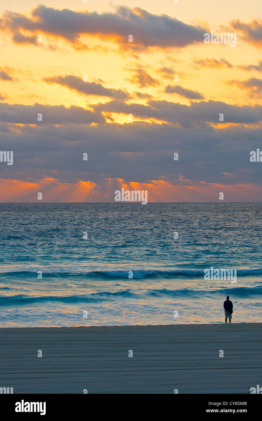 Person, die an einem Strand gerade Morgen Sonnenstrahlen brechen durch die Wolken (Hochformat) Stockfoto