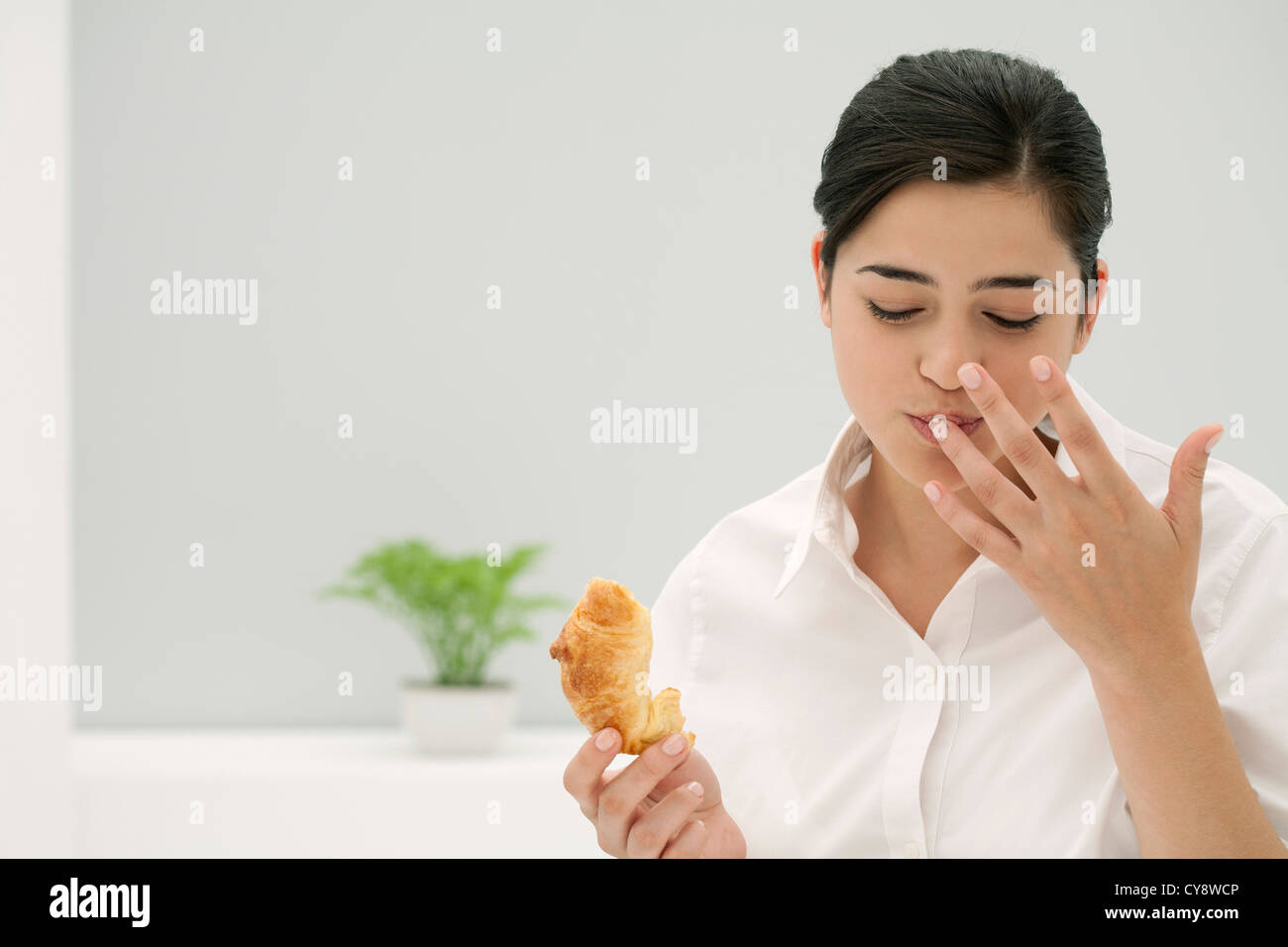 Junge Frau lecken Finger während des Essens croissant Stockfoto