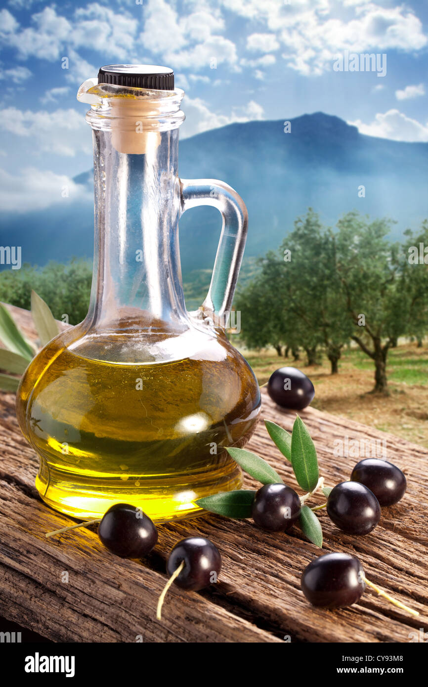 Schwarze Oliven mit Ölflasche auf einem Holztisch vor dem Hintergrund der Garten mit Olivenbäumen. Stockfoto