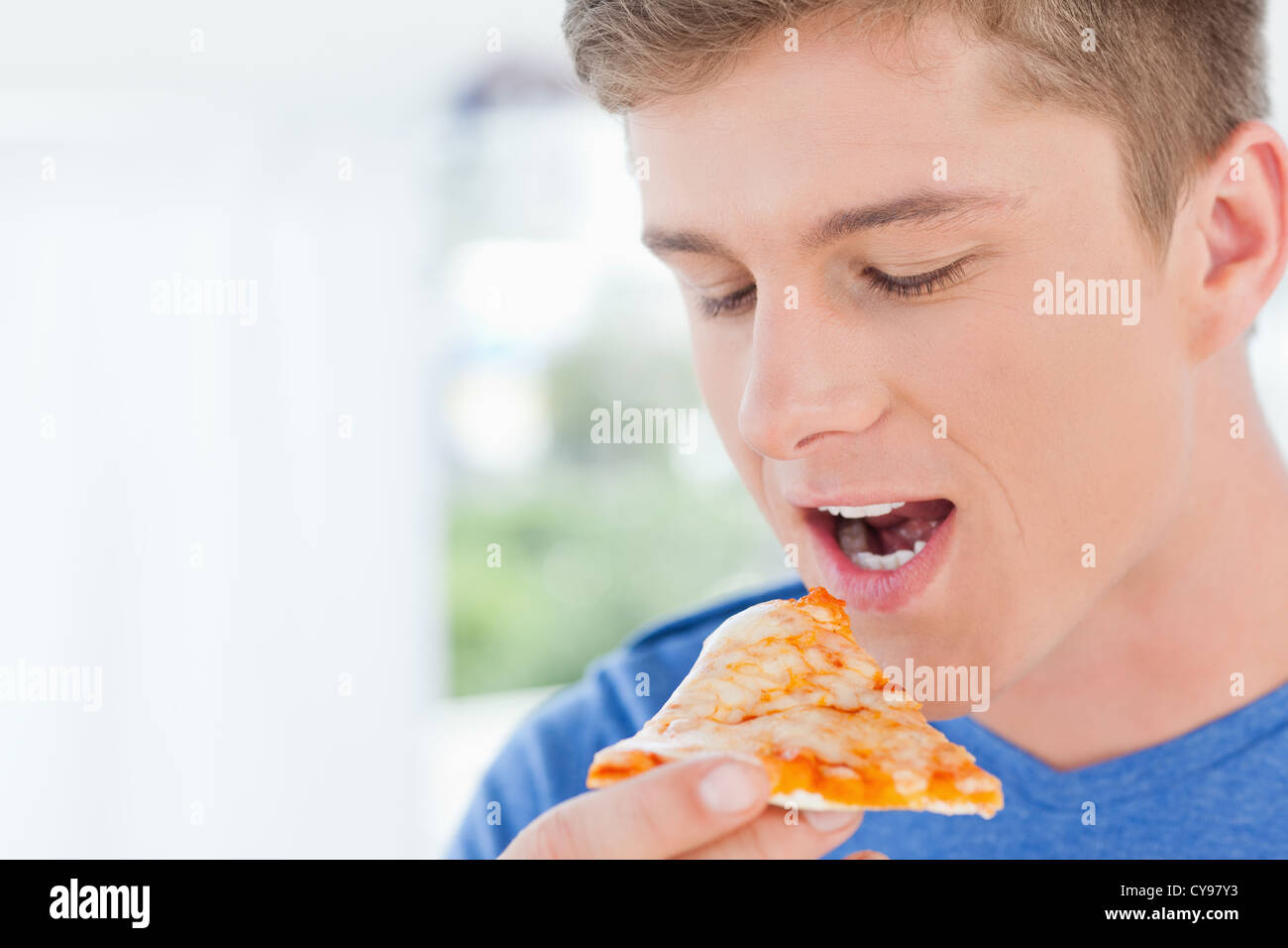 Ein Mann mit einem Stück Pizza in der Nähe seiner Mündung Stockfoto