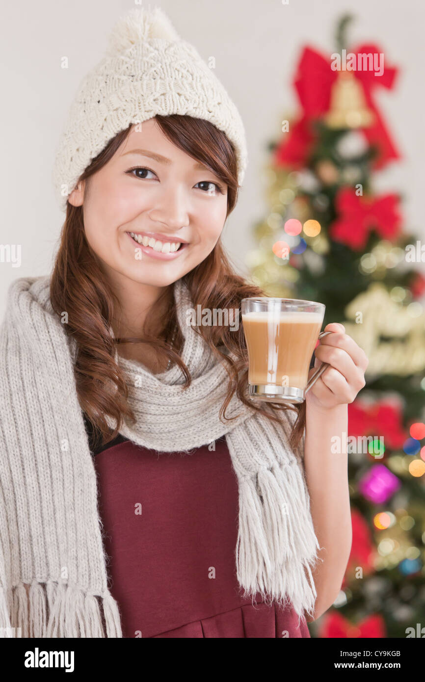 Young Woman Holding Cappuccinotasse vor Weihnachtsbaum Stockfoto