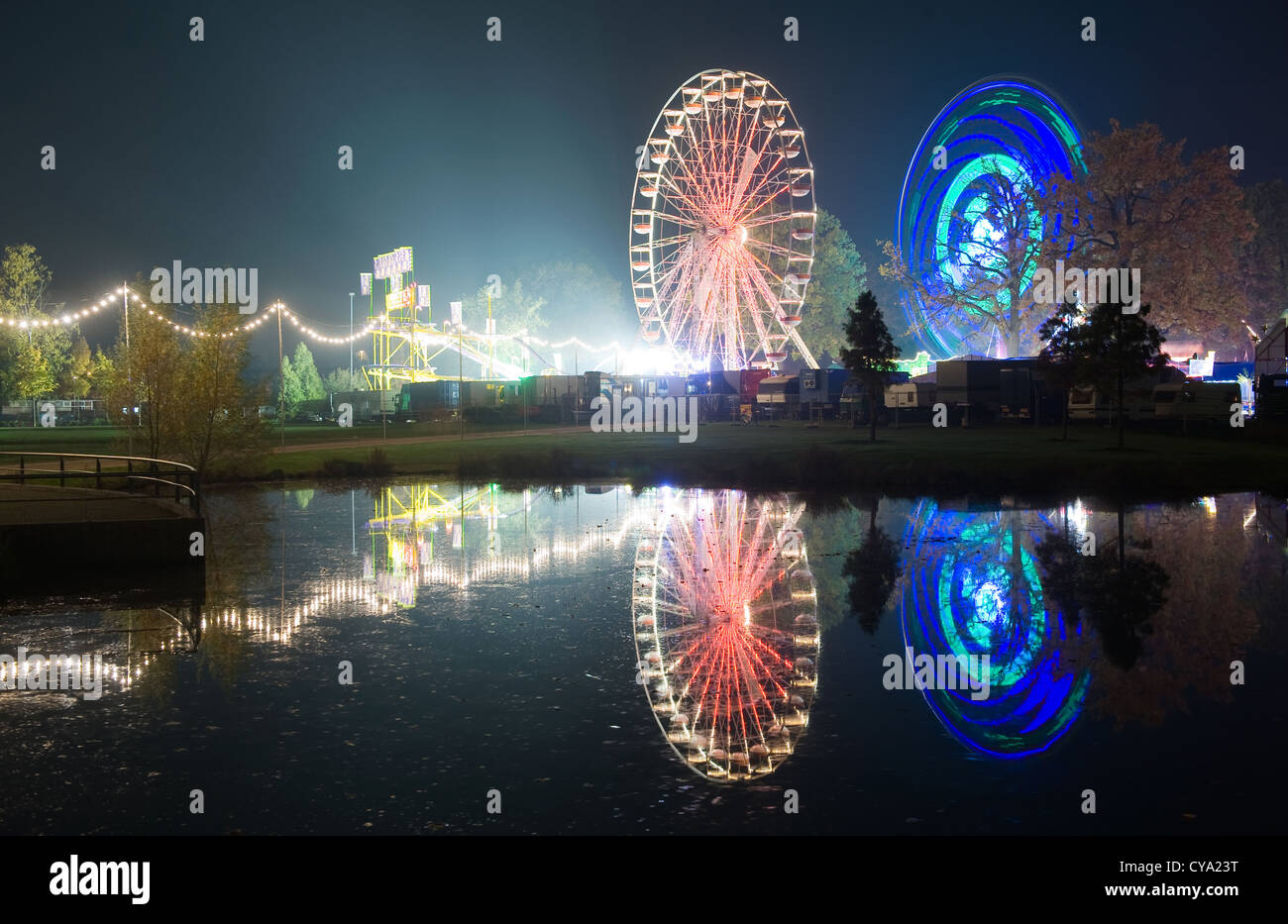Die Lichter von zwei Riesenräder in einem Vergnügungspark spiegelt sich im Wasser eines Teiches Stockfoto