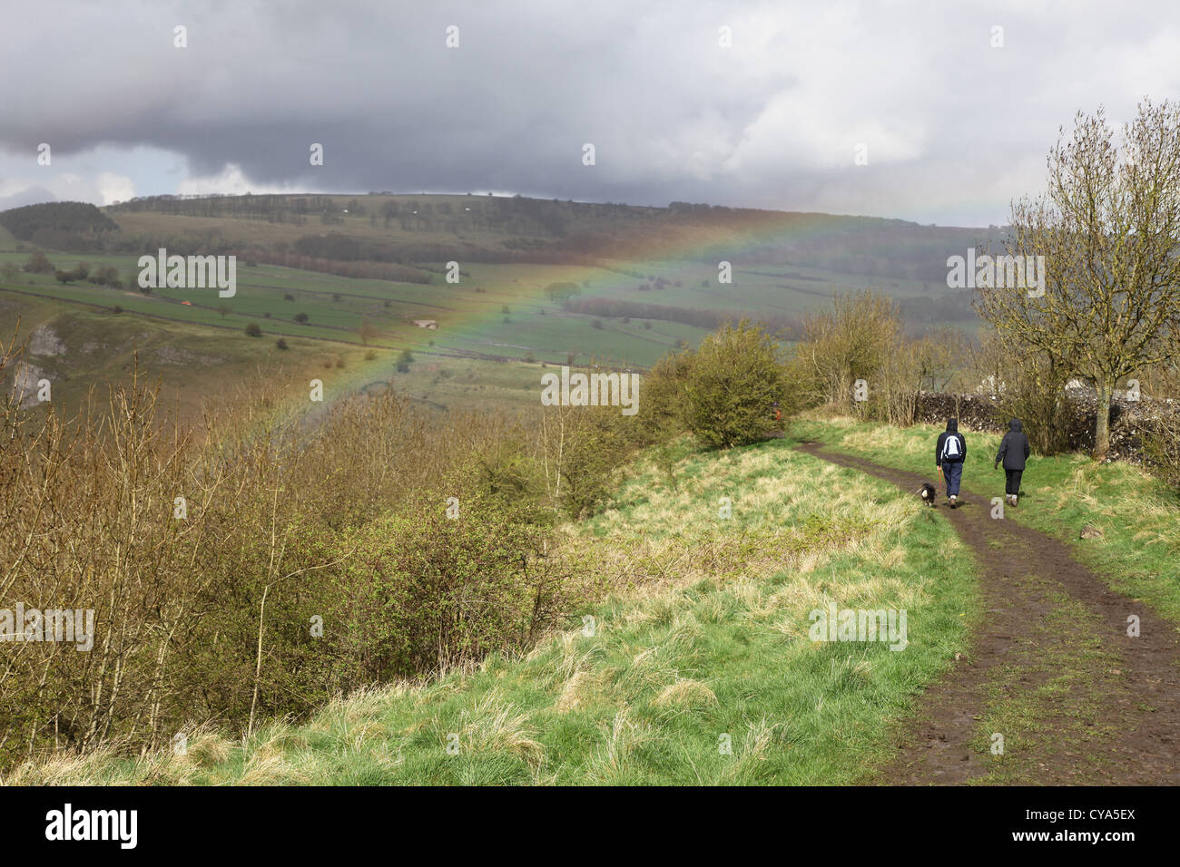 2 Wanderer und ein Hund zu Fuß in Monsal Dale Derbyshire White Peak District National Park England UK Regenbogen im Hintergrund Stockfoto