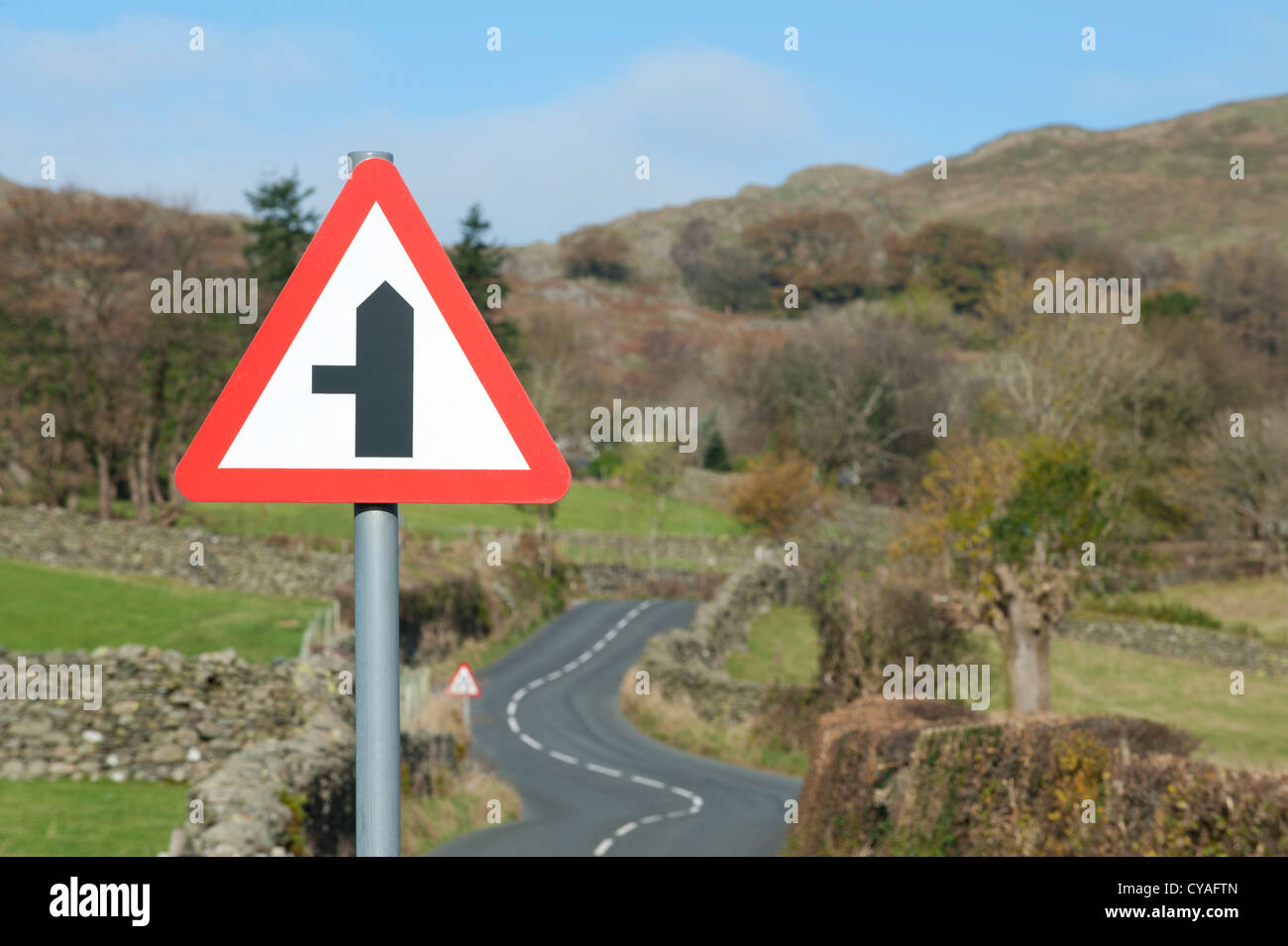 Ein Schild kennzeichnet eine Straße auf der linken Seite befindet sich eine kurvenreiche Landstraße in Lake District, Cumbria, England. Stockfoto