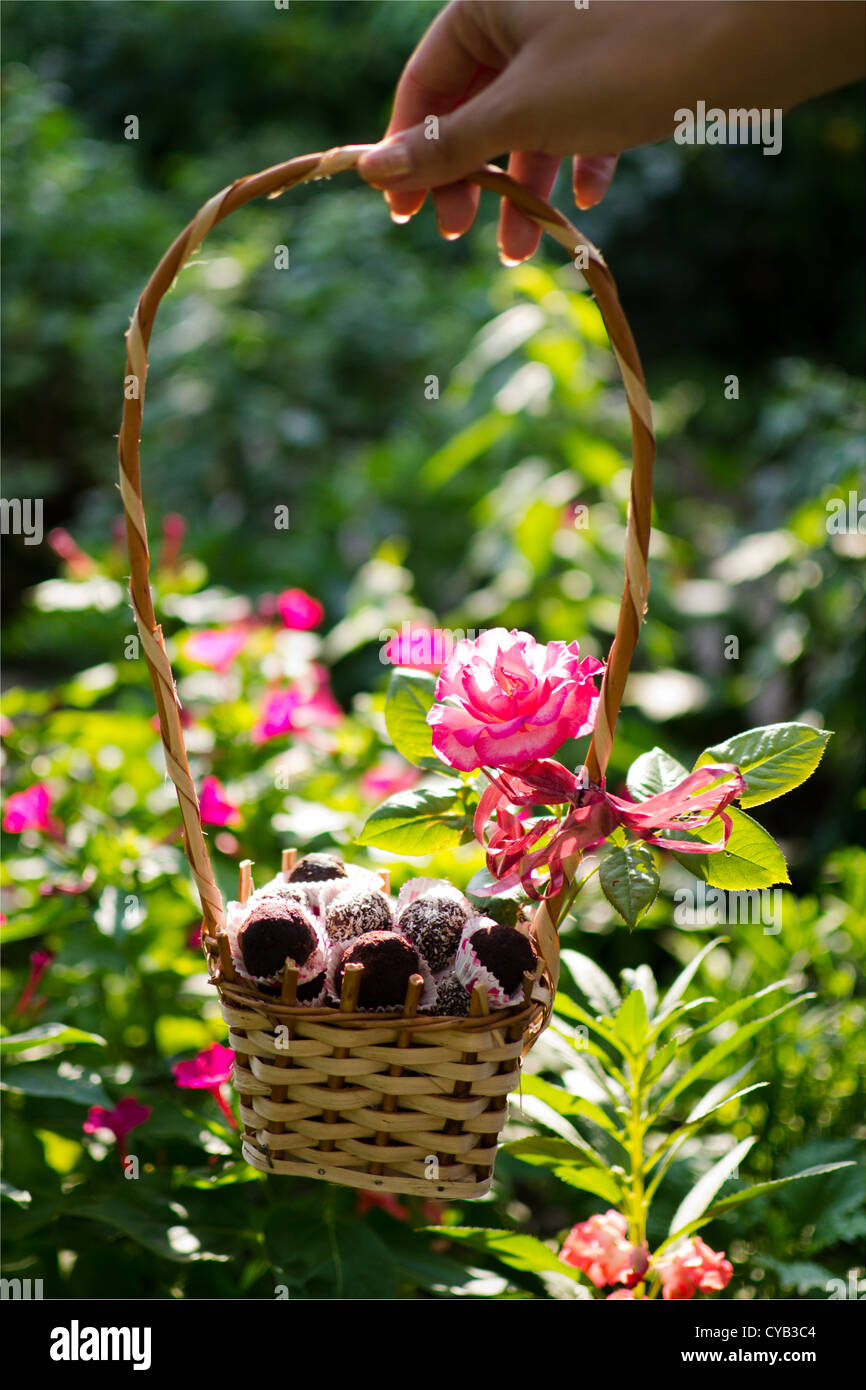 Hausgemachte Pralinen in einem Korb mit Blumen im Hintergrund. Stockfoto