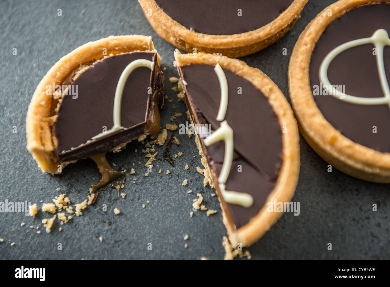 Drei Schokolade Törtchen von oben auf eine Schieferoberfläche gedreht. Eine Torte wurde mit Krümel und klebrige Karamell geschnitten. Stockfoto