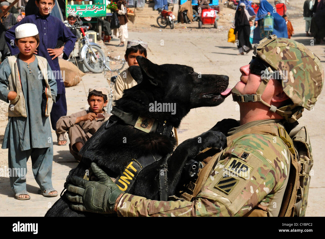 Ein Sergeant der US-Armee bekommt einen neuen Anstrich vertragen von seinen militärischen Gebrauchshund, Nero wie Kinder vor Ort in der Stadt Kandahar, Afghanistan am 3. Oktober 2012 aussehen Stockfoto