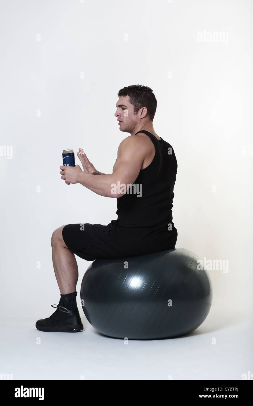 Mann sitzt auf einem Gymnastikball nicht sicher, ob er ein Bier statt Beendigung seines Trainings Stockfoto