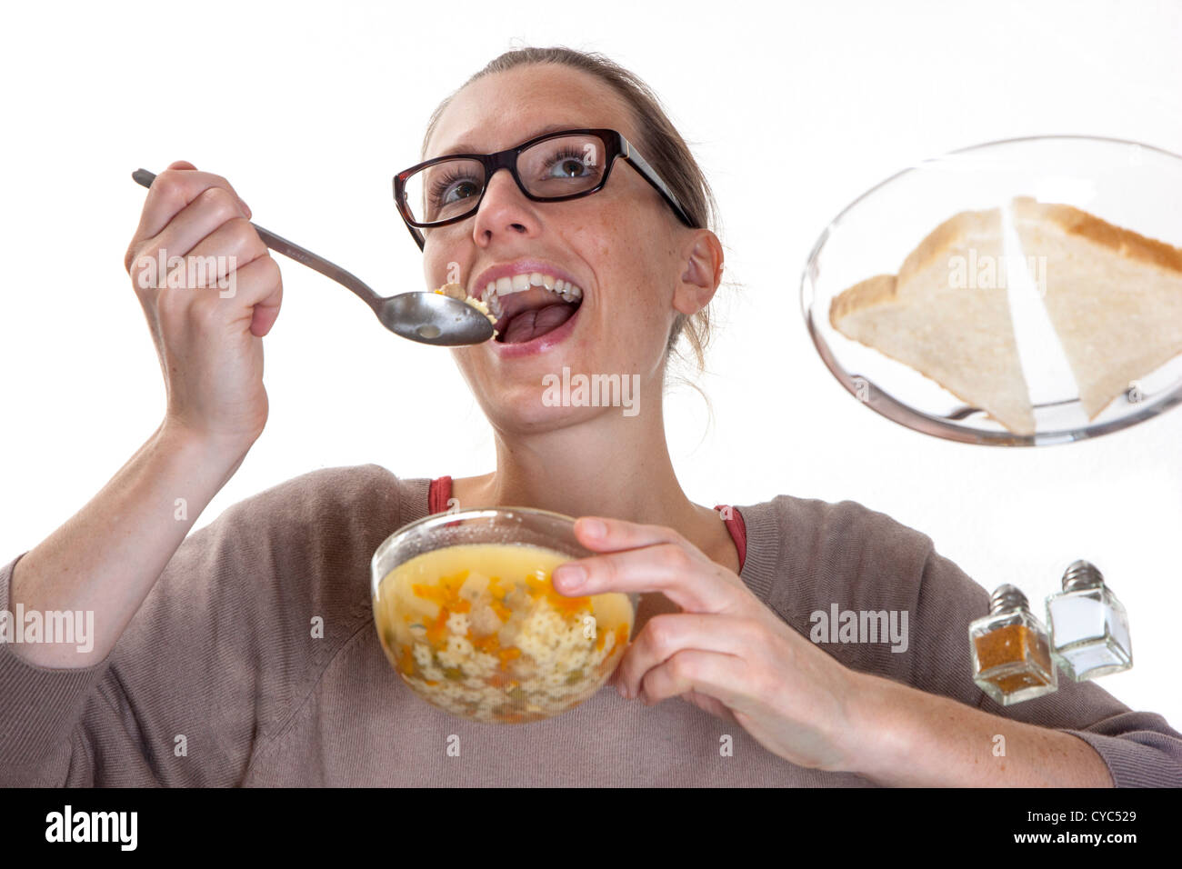 Junge Frau sitzt an einem Glastisch, Essen eine Suppe, Gemüse, Nudeln. Stockfoto