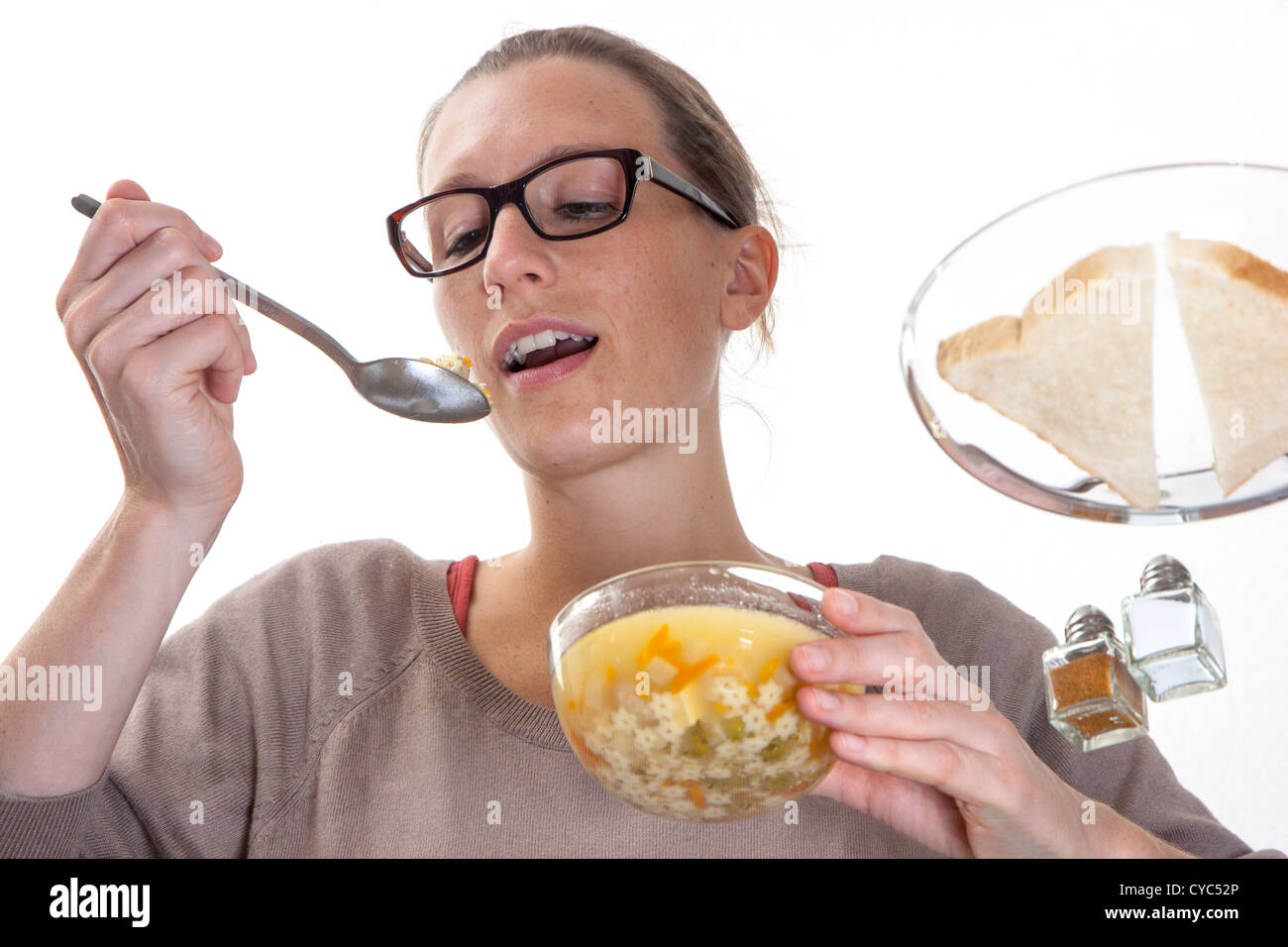 Junge Frau sitzt an einem Glastisch, Essen eine Suppe, Gemüse, Nudeln. Stockfoto