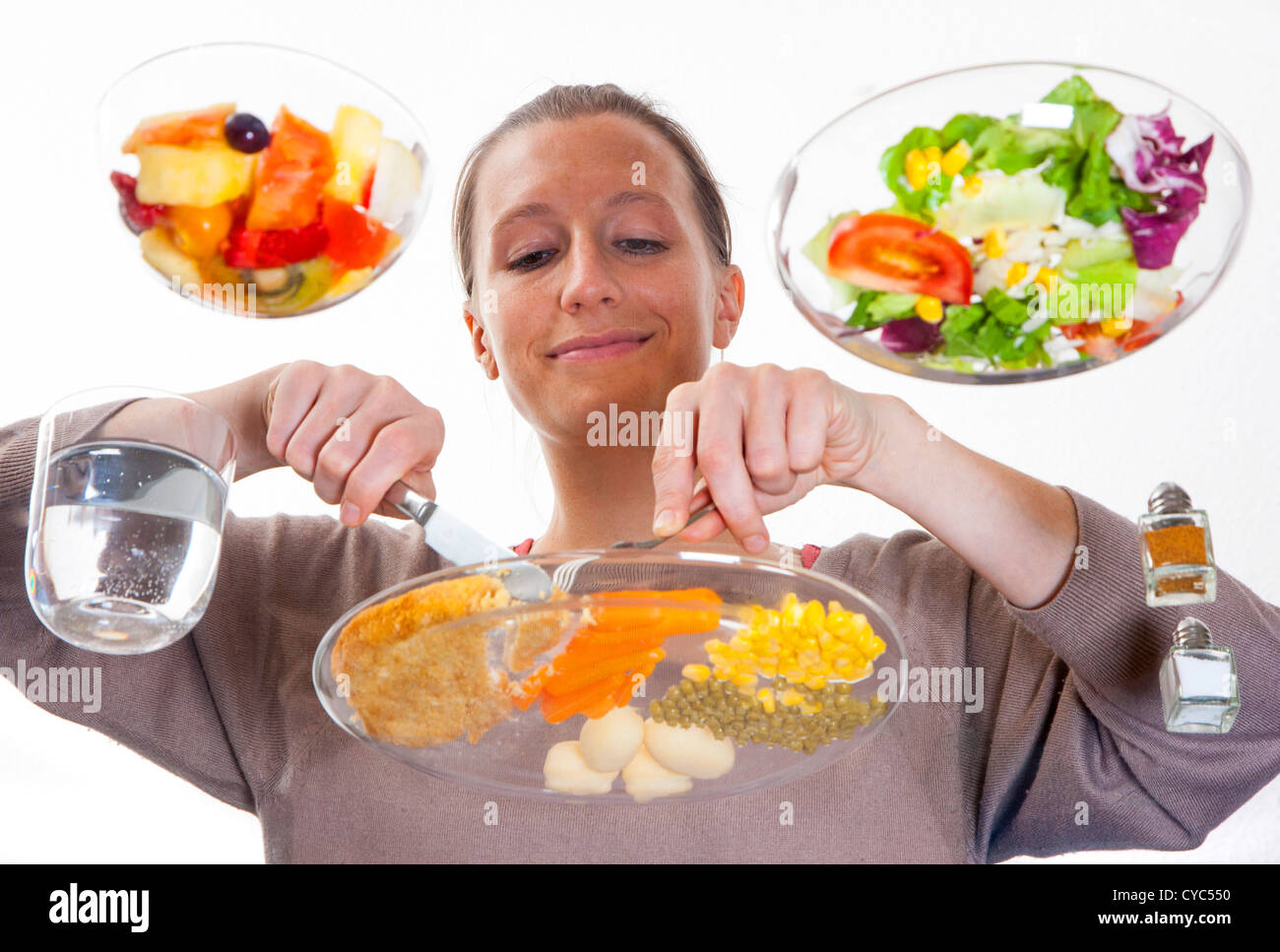 Junge Frau sitzt an einem Tisch aus Glas. Essen eine Mahlzeit, Schnitzel, Kartoffeln, Gemüse, gemischter Salat, Obstsalat, Wasser. Stockfoto