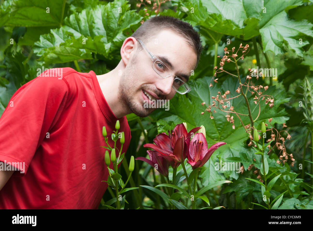 Mann in einem Garten biegen um Lily zu riechen und Blick in die Kamera Stockfoto