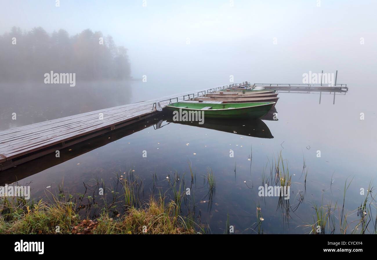 Kleine hölzerne Pier mit Booten auf See in kalten, nebligen Morgen Stockfoto