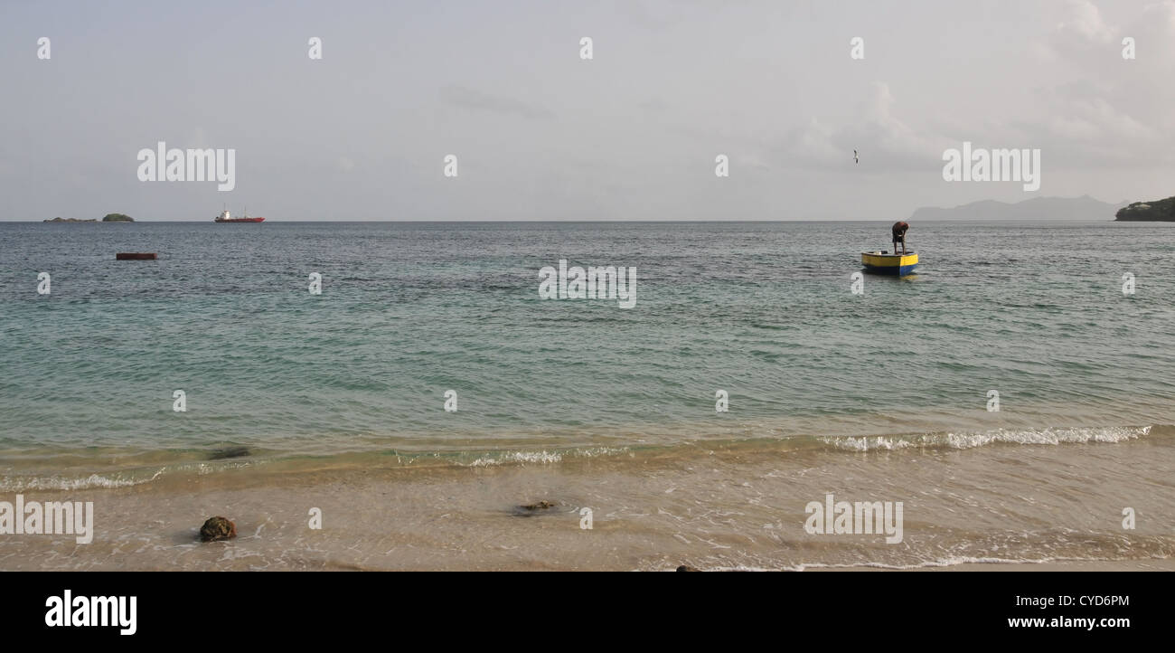 Ansicht, seewärts nach Union Island, Mann beugt gelb bemalten kleinen Fischerboot, Hillsborough Bay, Carriacou, West Indies Stockfoto