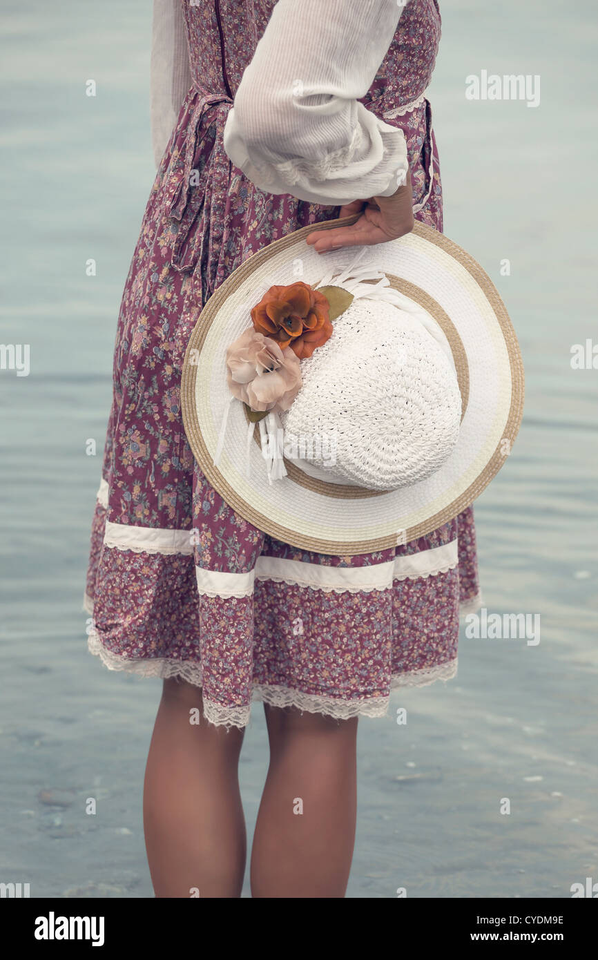 eine Frau in einem geblümten Kleid hält einen Strohhut Stockfoto