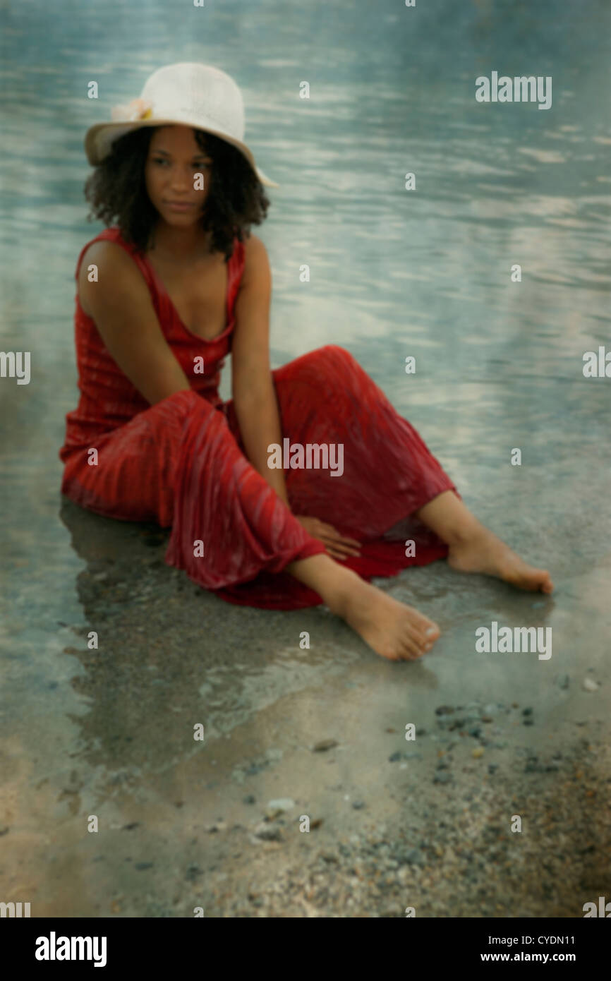 eine Frau in einem roten Kleid sitzt auf den Rand des Wassers Stockfoto