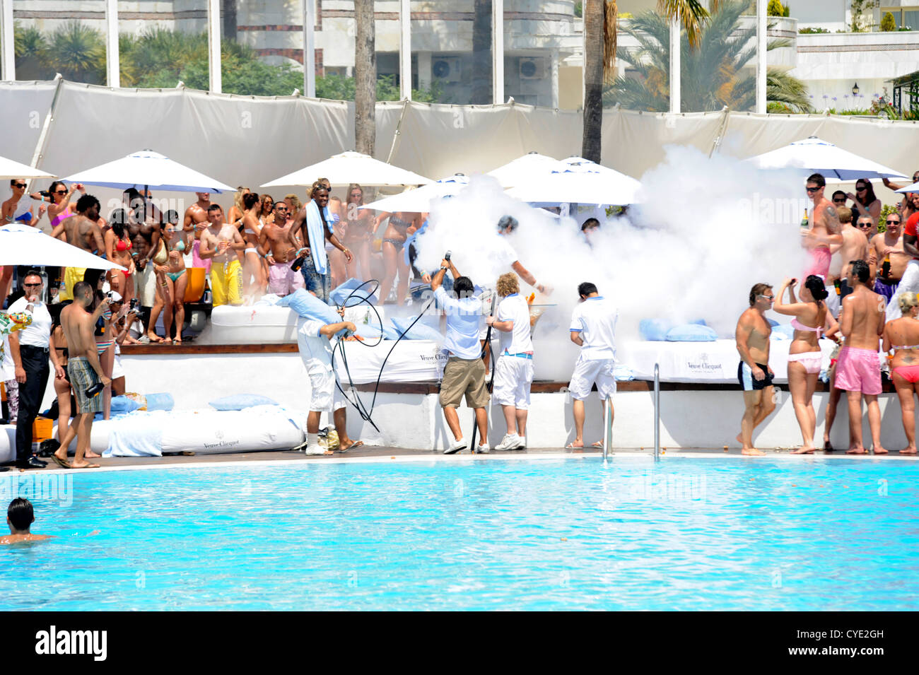 Kellner, die Bereitstellung von großen Flaschen Champagner für Kunden Sonnenliegen am Pool-Party, mit vielen weißen Rauch freigesetzt Stockfoto