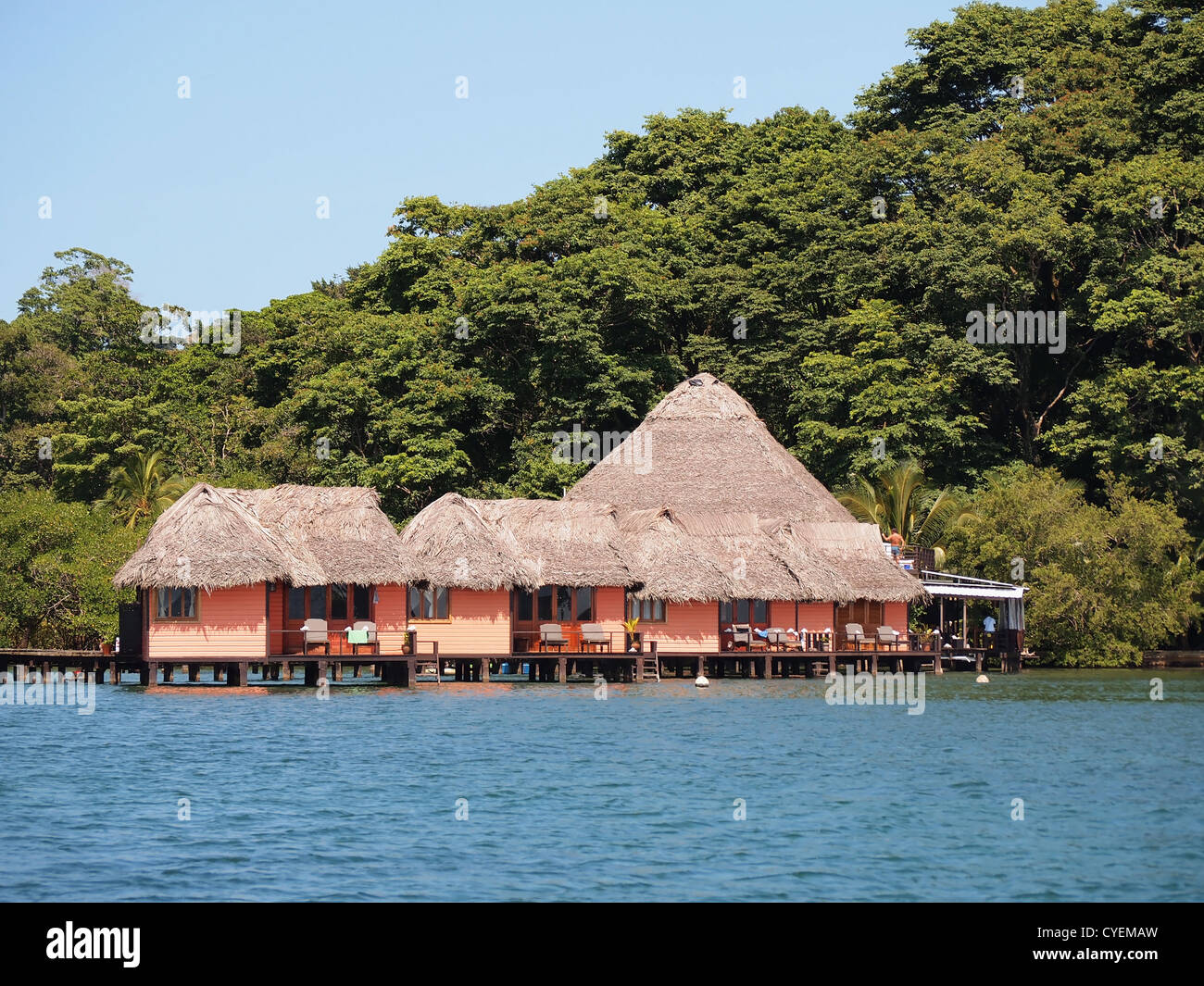 Tropisches Resort mit strohgedeckten Bungalows über dem Wasser und üppige Bäume im Hintergrund, Mittelamerika, Panama Stockfoto