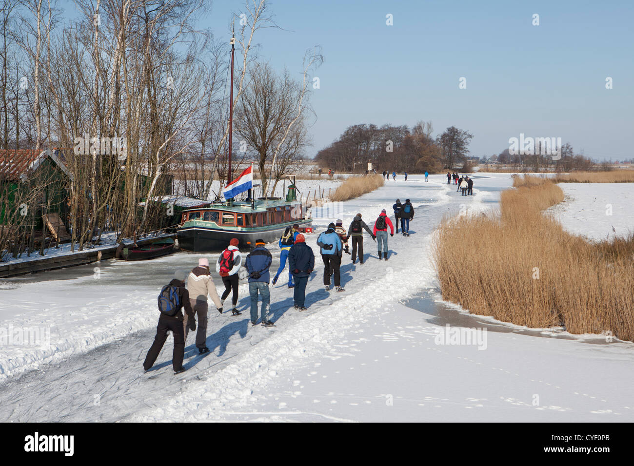 Niederlande, Jisp, Winter. Menschen Sie Eislaufen auf dem Polder Kanal vor Bauernhof und Hausboot. Stockfoto