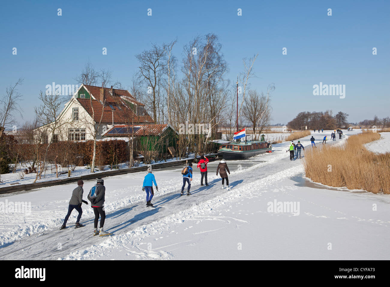 Niederlande, Jisp, Winter. Menschen Sie Eislaufen auf dem Polder Kanal vor Bauernhof und Hausboot. Stockfoto