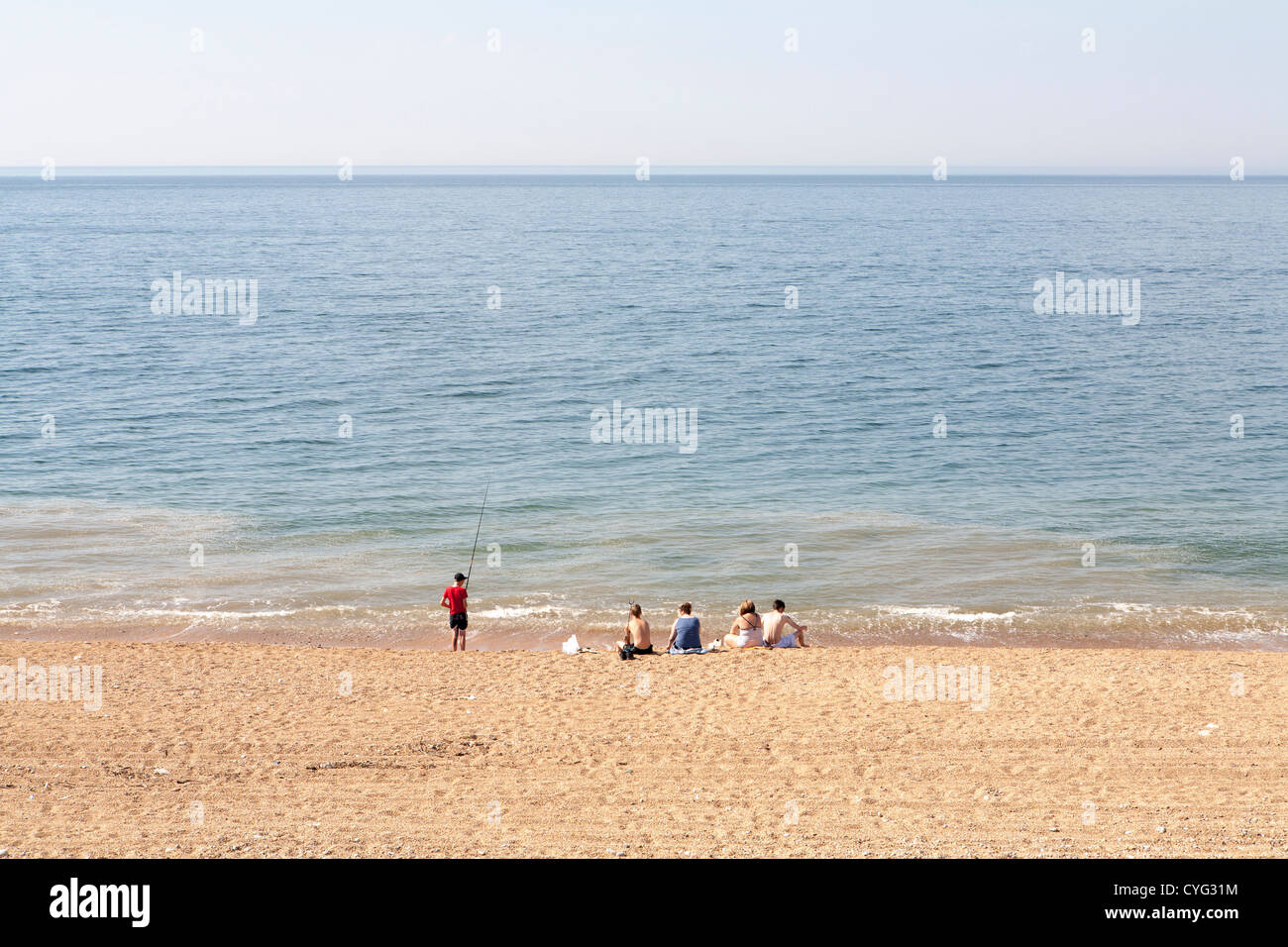 Gruppe junger Leute sitzen am Strand von UK mit einer holding eine Angelrute Stockfoto