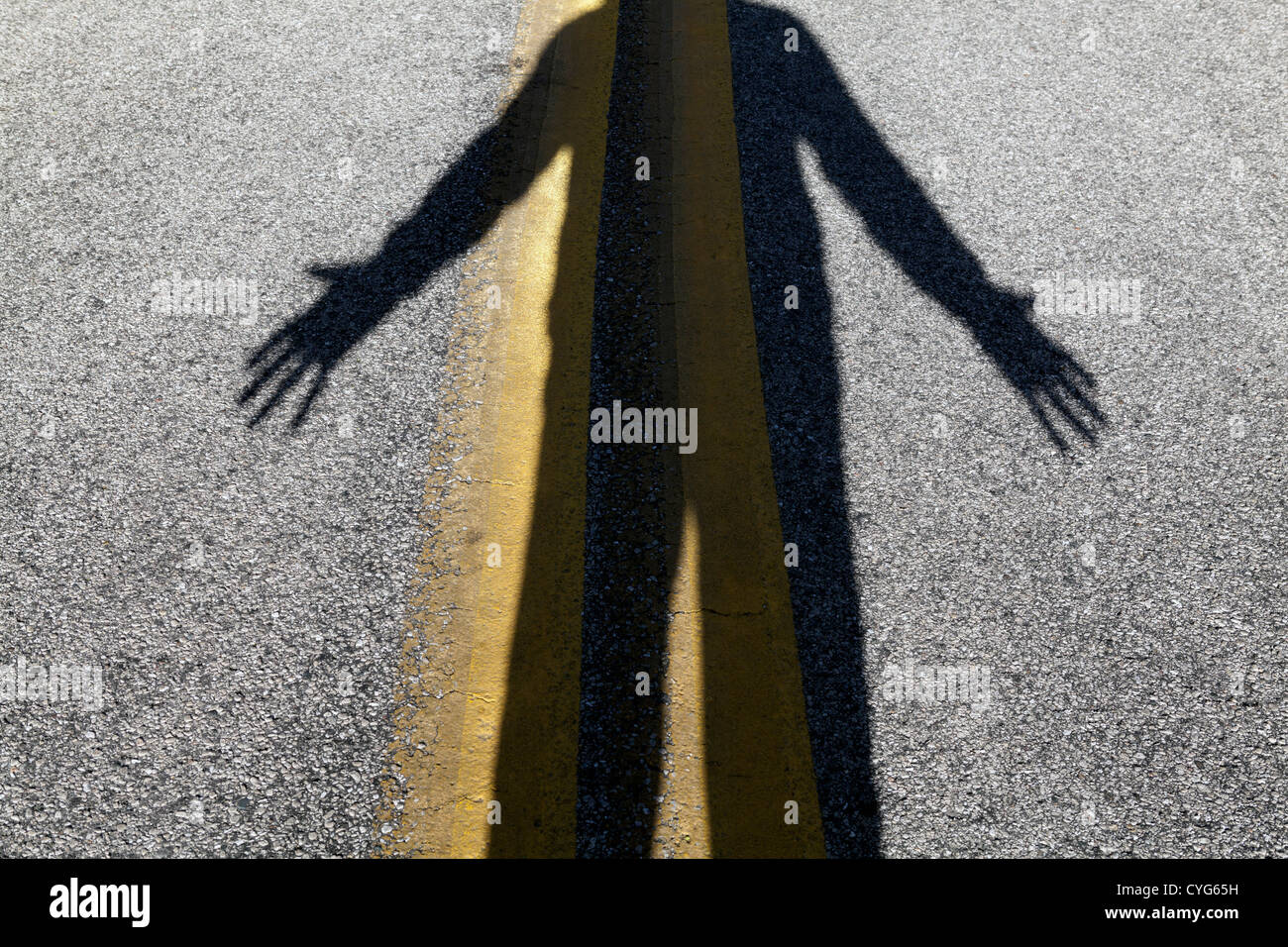 Ein beängstigender Schatten einer menschlichen Figur liegt auf den gelben Linien einer Straße. Stockfoto