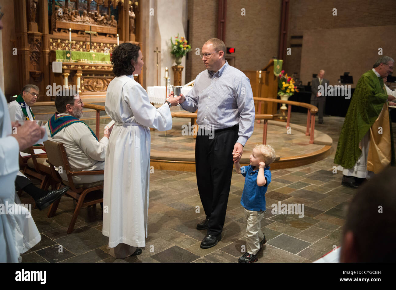 Frau im Alb präsentiert Kommunion Wein Gemeinde Mitglied und seinem kleinen Sohn beim Service in der lutherischen Kirche Stockfoto