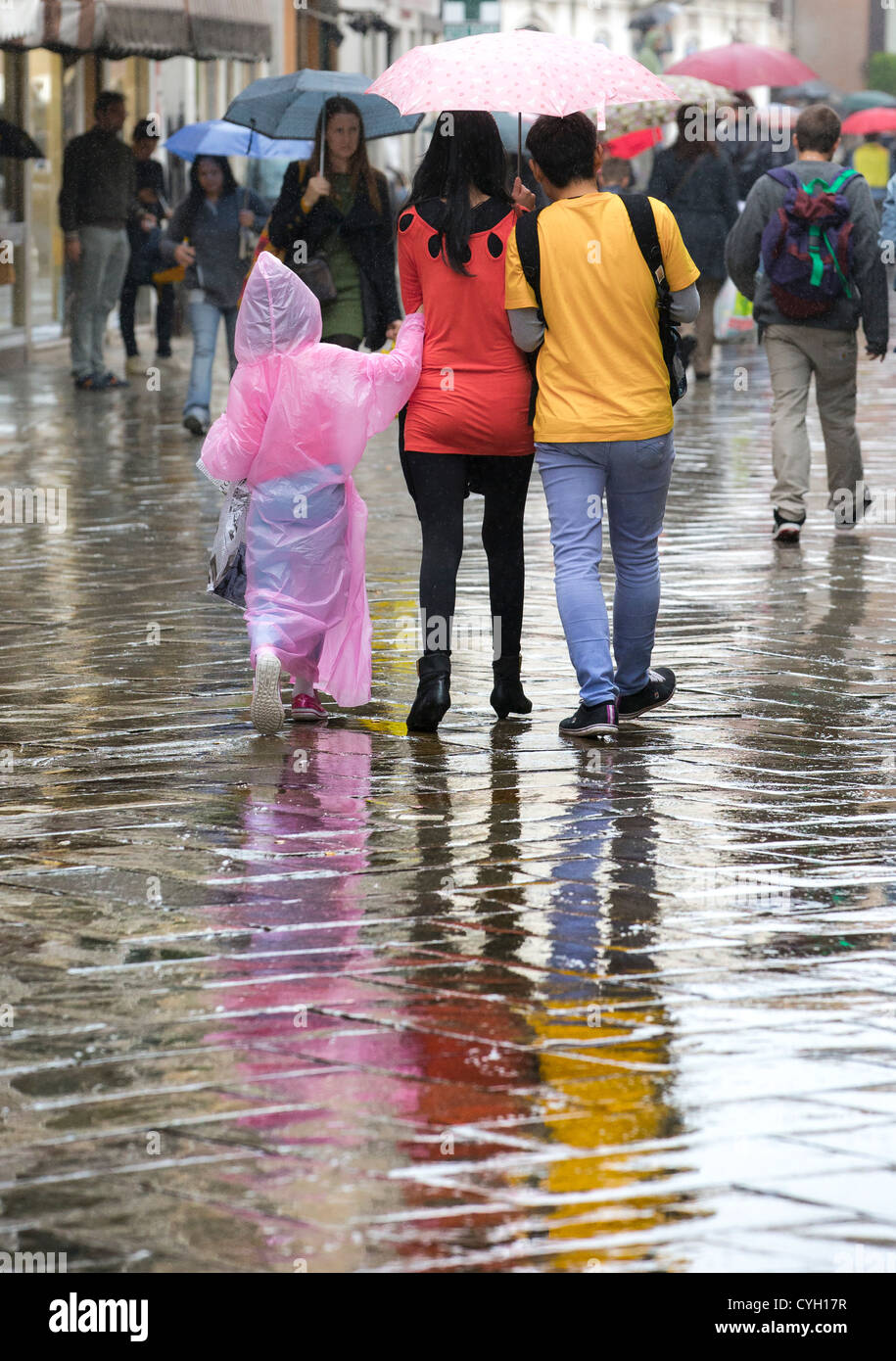 Ein paar Wandern in den Regen unter einem rosa Regenschirm mit einem Kind in einem langen rosa wasserdichte Umhang Stockfoto