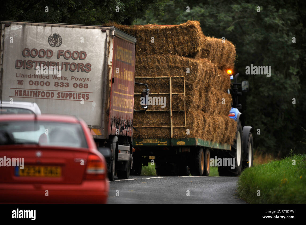 Verkehr stecken hinter einem Traktor mit einem Anhänger von Heu auf einer Straße in Gloucestershire UK Stockfoto