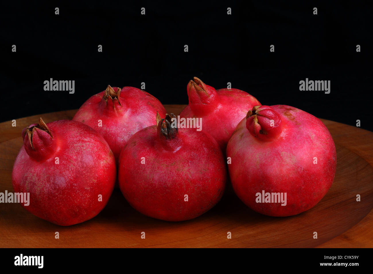 Nahaufnahme von fünf Granatäpfel auf einer hölzernen Platte und einem schwarzen Hintergrund. Querformat. Stockfoto