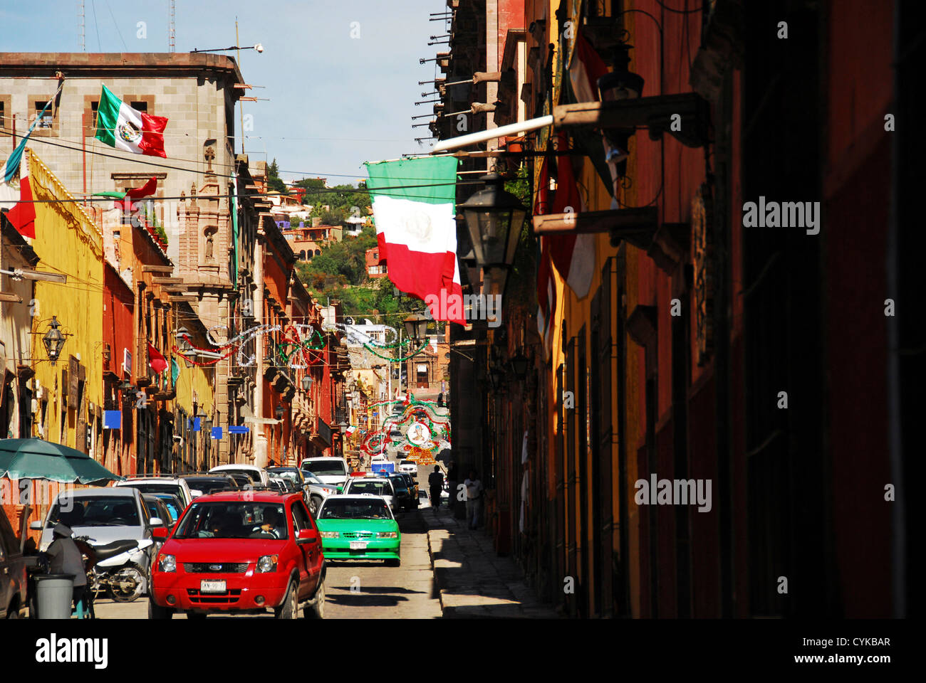Mexiko, San Miguel de Allende, Flagge schmeichelhaft an Gebäuden, Auto bewegen auf Straße inmitten von Gebäuden Stockfoto