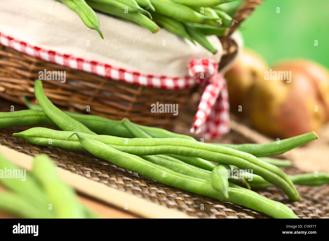 Frische rohe grüne Bohnen vor einem Korb mit Kartoffeln in den Rücken Stockfoto