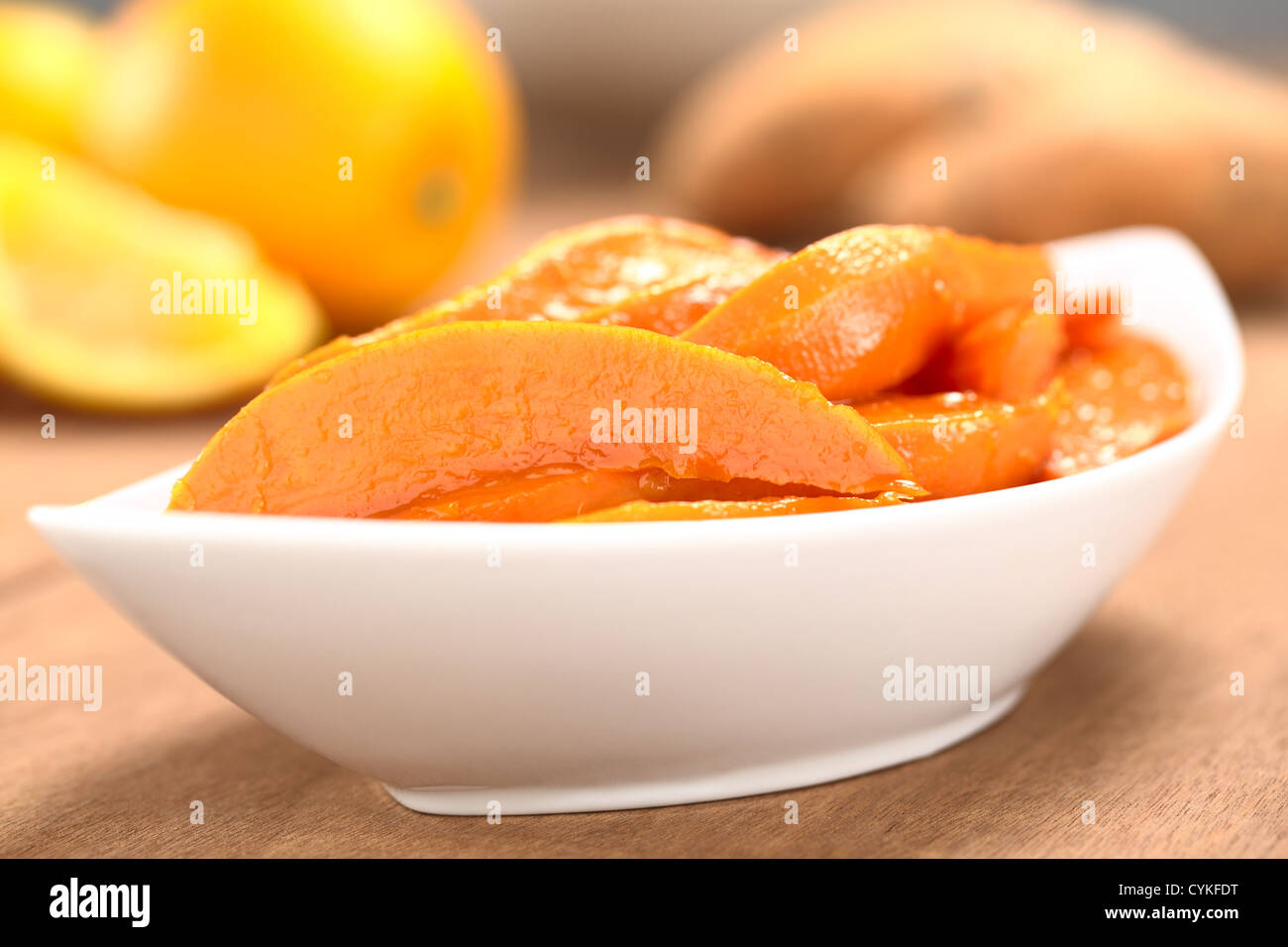 Schüssel von Sweet Potato Wedges karamellisiert mit braunem Zucker und frisch gepressten Orangensaft mit Süßkartoffeln und Orangen in den Rücken Stockfoto