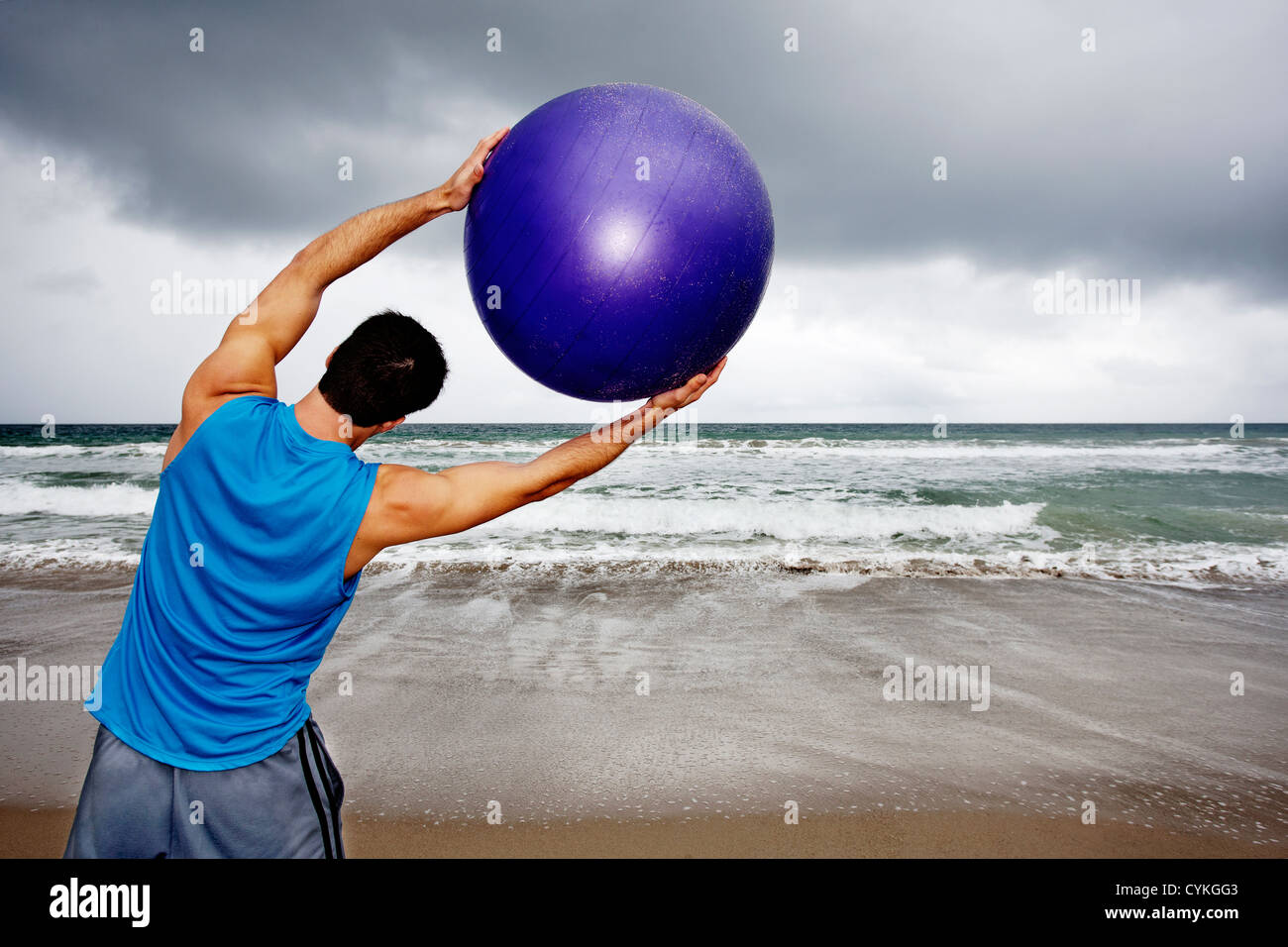 Junger Mann hält Gymnastikball am Strand Stockfoto