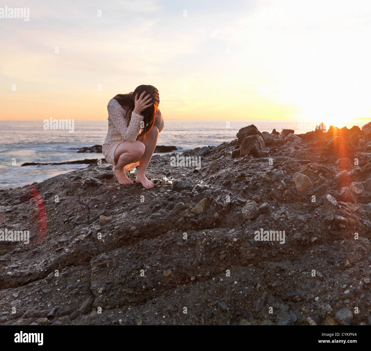 Frau hält ihren Kopf auf felsigen Strand Stockfoto