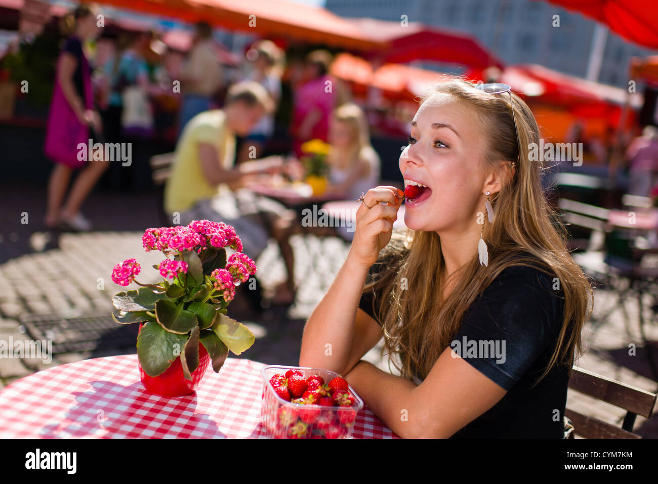 Schönes Mädchen sitzt auf dem Markt-Café und sie essen leckere Erdbeeren Stockfoto
