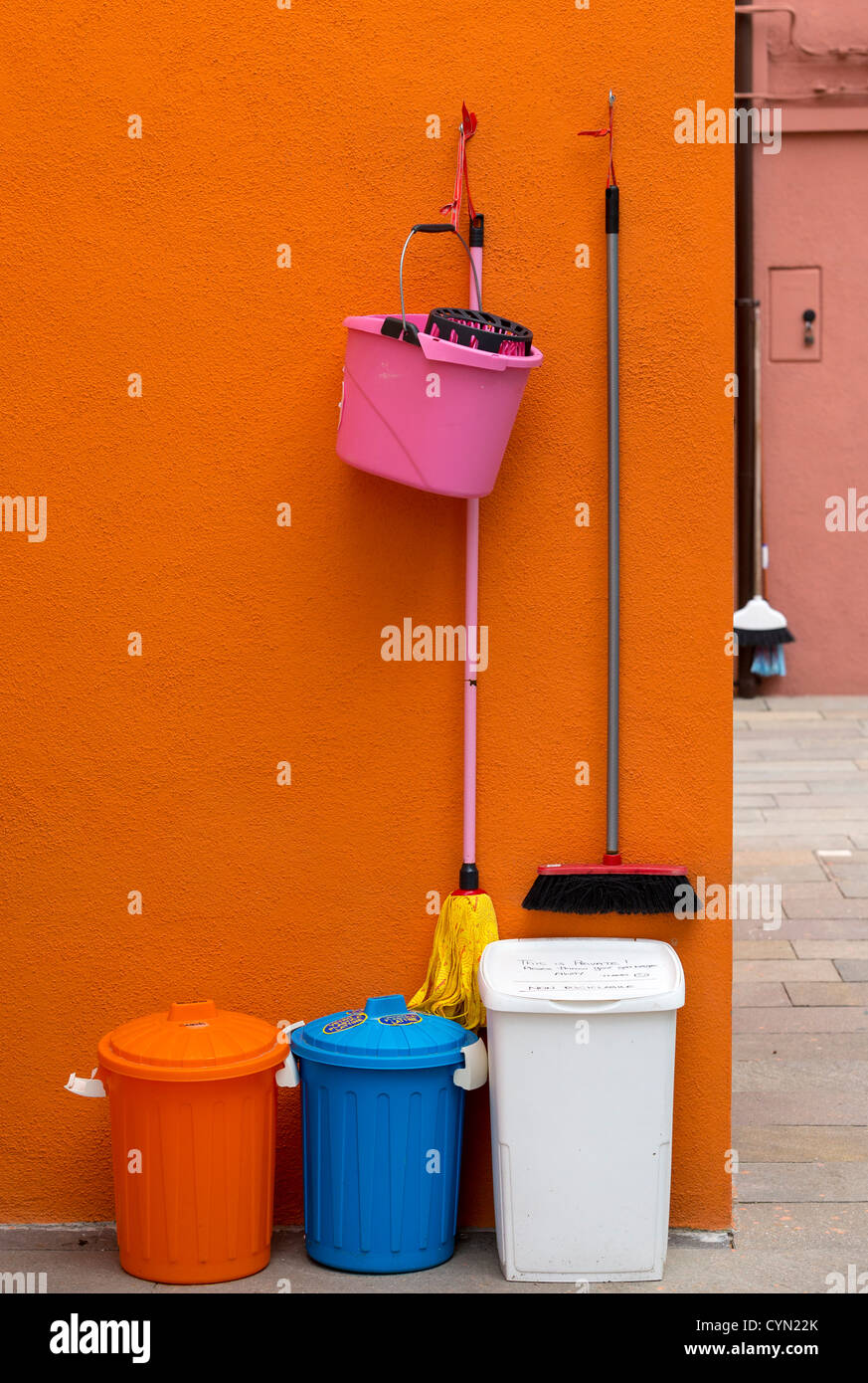 Bunten Kästen, ein Eimer, Mopp und fegen-Bürste gegen eine Orange Wand in Burano, Venedig. Stockfoto