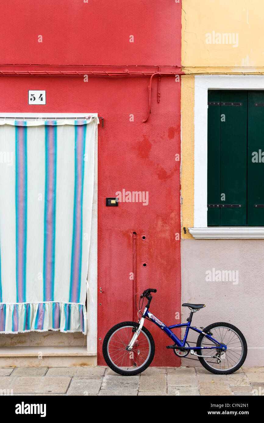 Blaue Fahrrad steht vor einem tiefen rot lackierten Haus mit einem rosa, blau und weiß gestreifte Vorhang Stockfoto