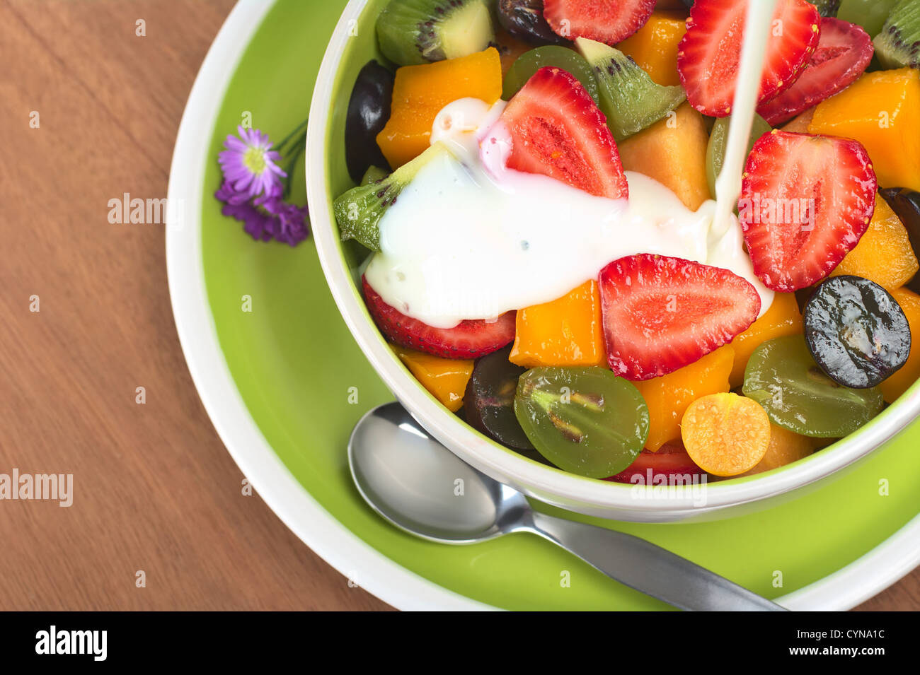 Frisches und gesundes Obstsalat mit Erdbeeren, Kiwi, Trauben, Mango und Physalis in einer Schüssel mit Joghurt übergossen wird Stockfoto