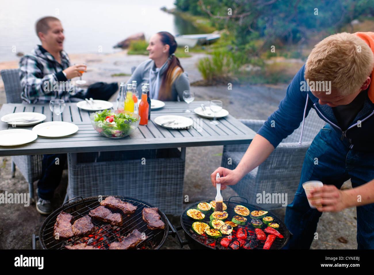 Fleisch und Gemüse in Grill, junges Paar lachend auf Hintergrund Stockfoto