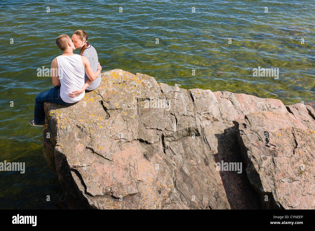 Junge Liebhaber sitzen und auf dem großen Felsen küssen Stockfoto