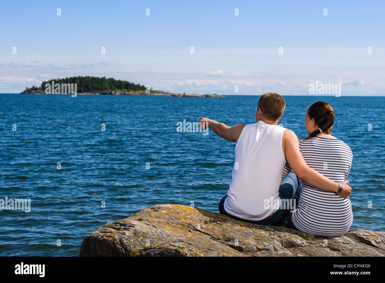 Junge Paar auf großen Felsen sitzen und sie sehen fern am Meer Stockfoto