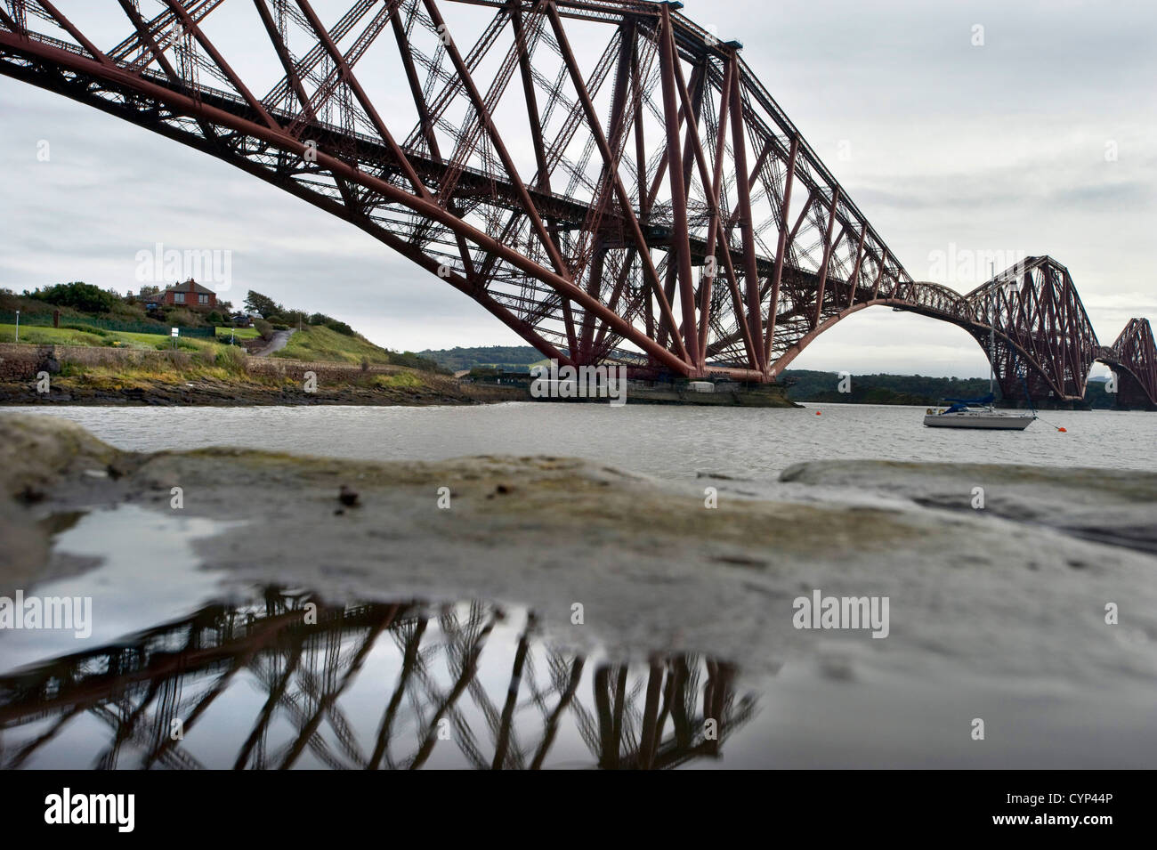 Die Forth Bridge spiegelt sich in einer Pfütze auf dem North Queensferry Ufer des Firth of Forth Stockfoto