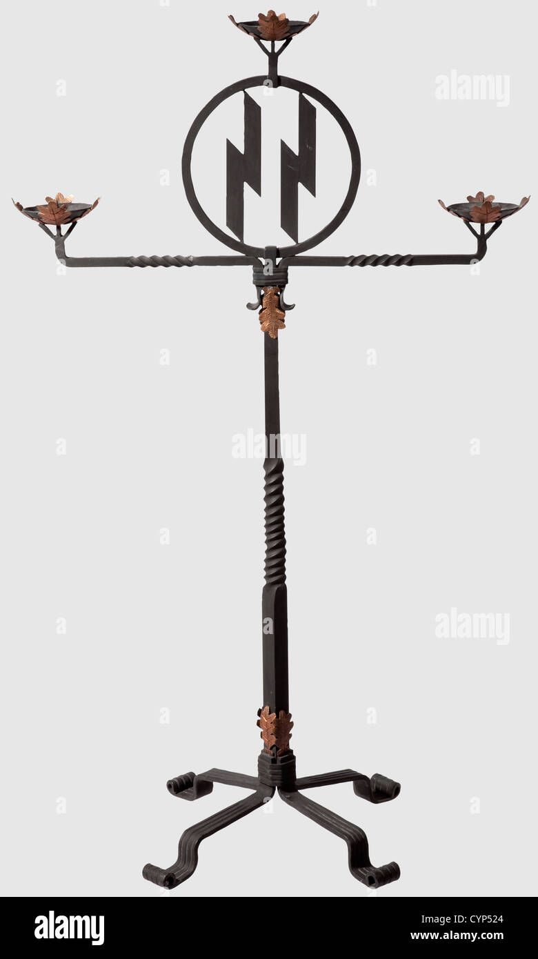Ein schmiedeeiserner SS Hochzeitskandelaber, geschwärztes Eisen mit handgeprägten und gravierten Kupfereichenblättern verziert.Version mit drei Kerzenstäbchen, die Tropfschalen unterstützt von 'Lebensrunen', und mit durchbrochenen SS Runen in einem zentralen Medaillon.Kreuzförmige Basis.Höhe 109 cm.die 'Lebensrune' (Algiz Rune) ist das Emblem des Lebensborn Vereins, der 1935 gegründet wurde Instanz von Heinrich Himmler zur Unterstützung der großen Familien von SS-Angehörigen und der Betreuung bedürftiger Mütter und Kinder von 'gutem Blut' in geeigneten Häusern.der Hauptsitz der Le,Additional-Rights-Clearences-nicht verfügbar Stockfoto