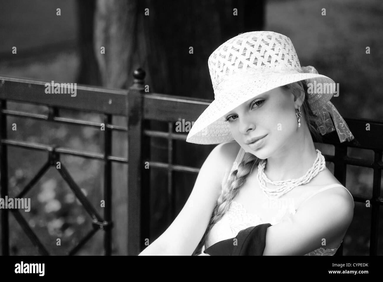 Junge Dame mit weißen Hut sitzt auf der Bank im park Stockfoto