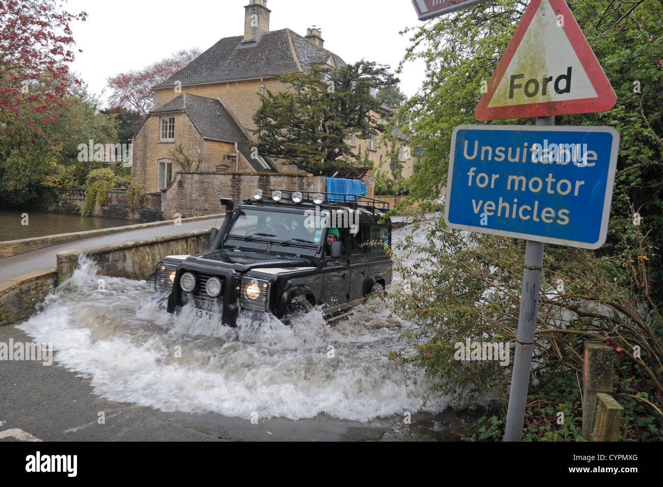 Ein Land Rover Defender beenden einen überfluteten Ford auf dem River Windrush, Bourton auf dem Wasser, Gloucestershire, UK. Stockfoto