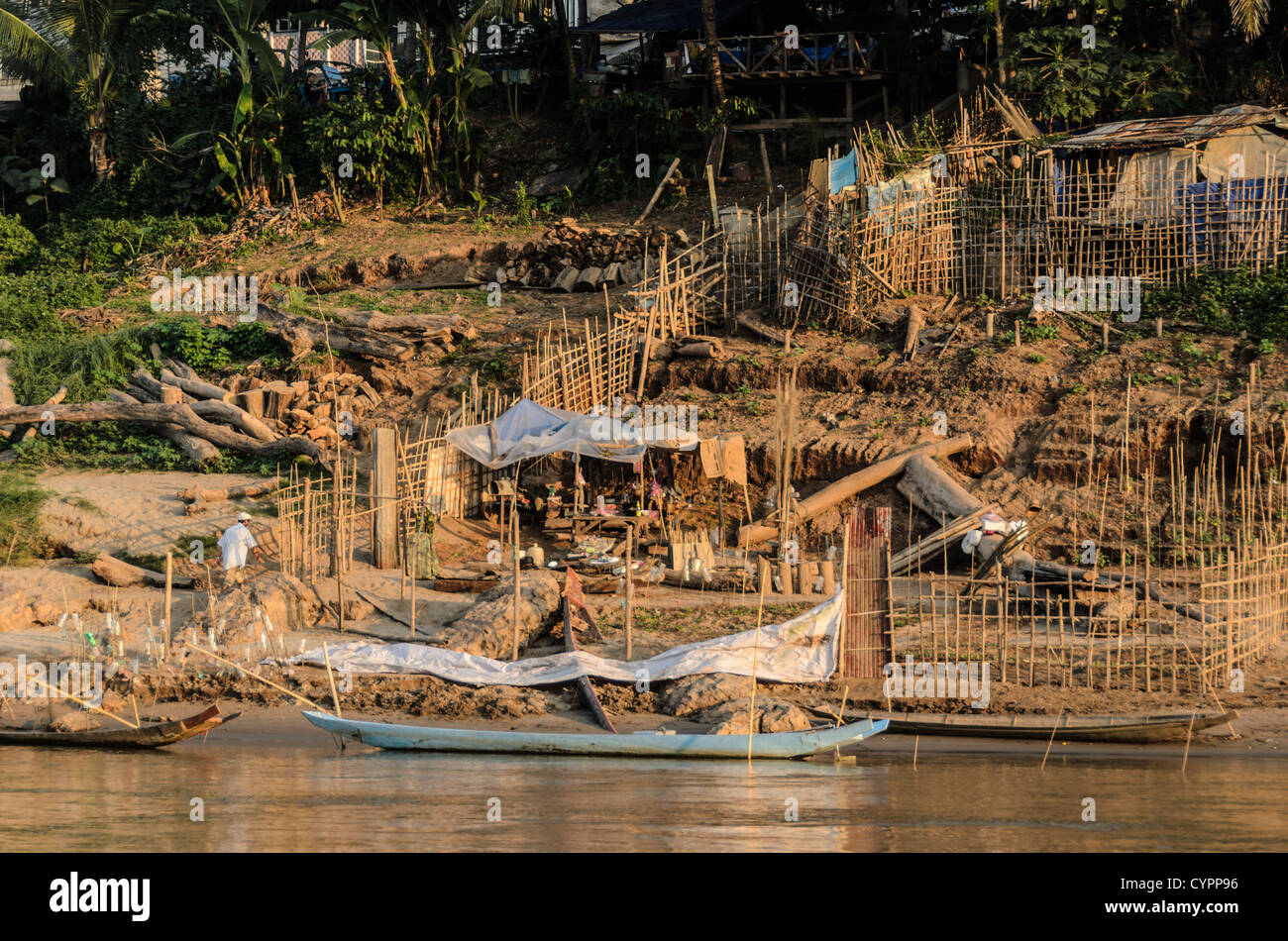 LUANG PRABANG, Laos — Ein einheimischer Landwirt bewirtschaftet einen kleinen provisorischen Bauernhof an den steilen, matschigen Ufern des Mekong-Flusses in der Nähe von Luang Prabang, Laos. Unter Ausnutzung der niedrigen Wasserstände der Trockenzeit nutzt der Landwirt das exponierte, fruchtbare Flussufer, um Nutzpflanzen anzubauen und traditionelle landwirtschaftliche Praktiken zu demonstrieren, die an die saisonalen Schwankungen des Mekong angepasst sind. Stockfoto