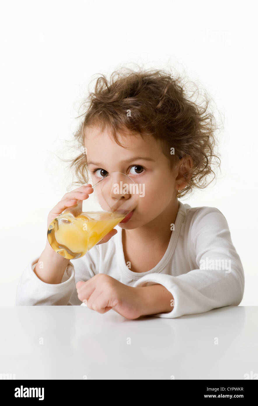 Kaukasische Mädchen, ca. 5-6 Jahre alt, braune Augen, lockiges Haar, trinkt ein Glas Orangensaft, isoliert auf weißem Hintergrund Stockfoto